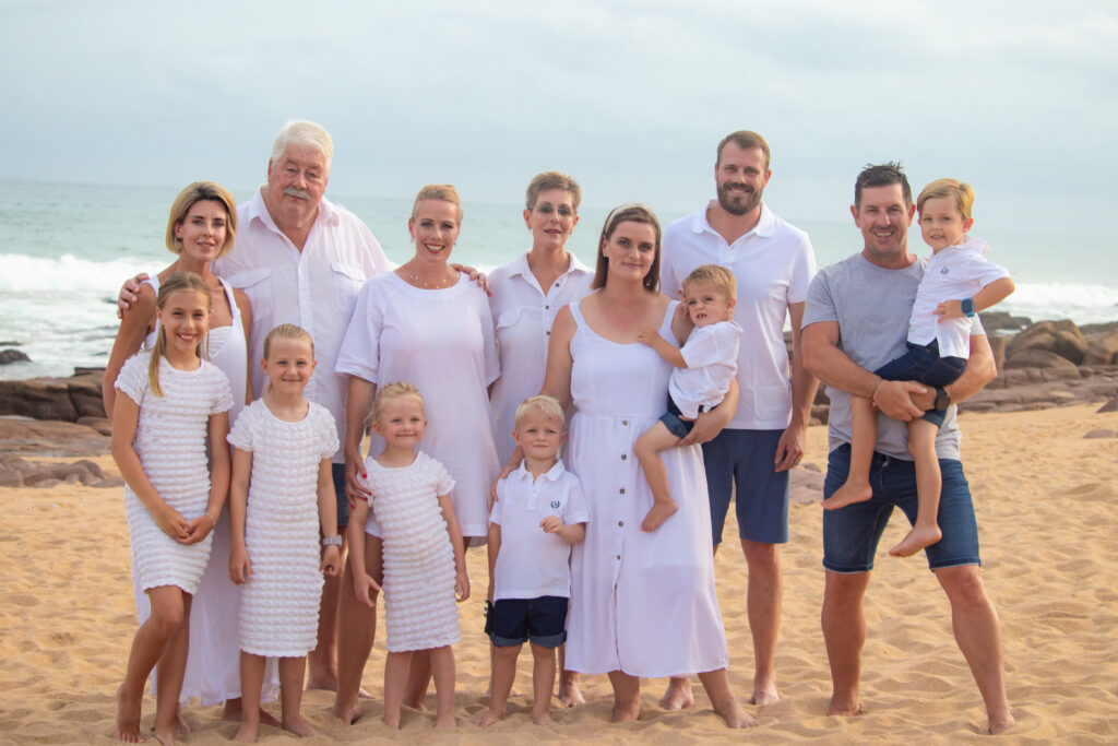 Big family group of adults and children standing next to each other on the beach